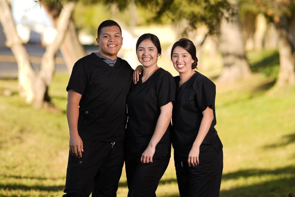 Group of students posing together in scrubs outside of school facility Group of students posing together in scrubs outside of school facility